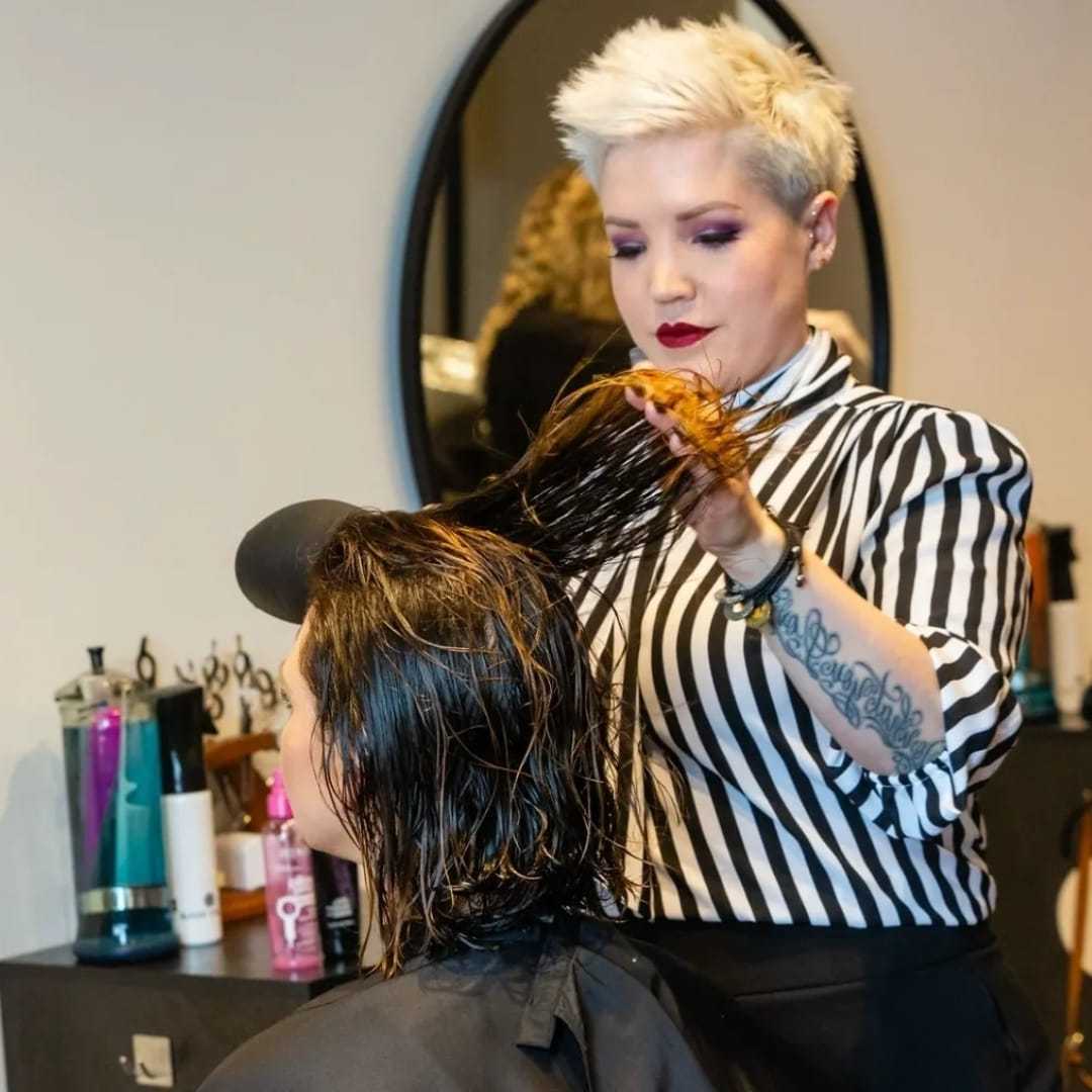 A hairstylist with short blonde hair cutting a client's wet hair in a salon.