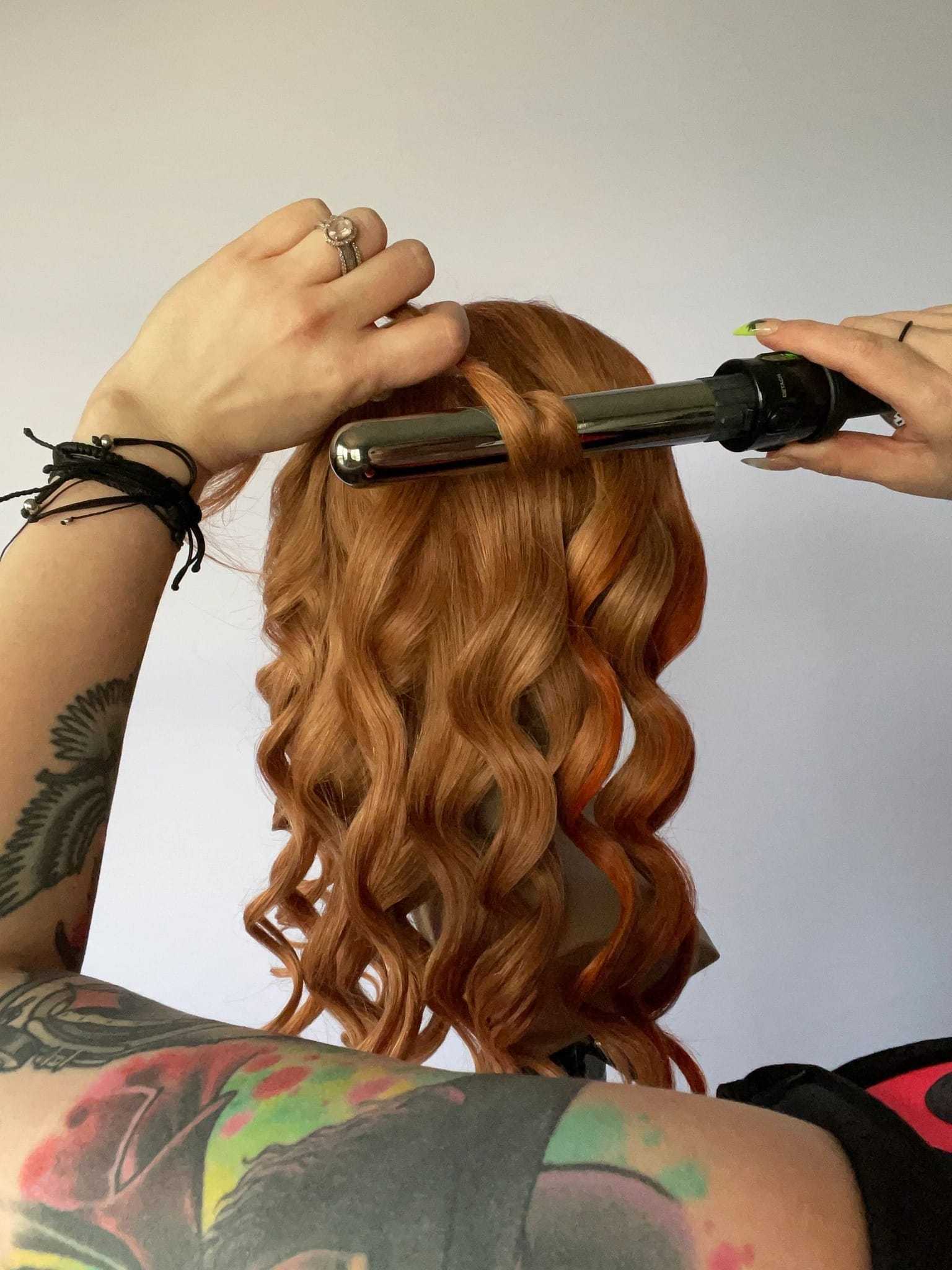 Stylist curling long red hair with a hot iron.