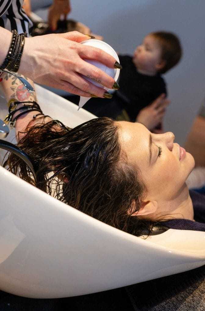 Person getting their hair washed at a salon, with a child playing in the background.